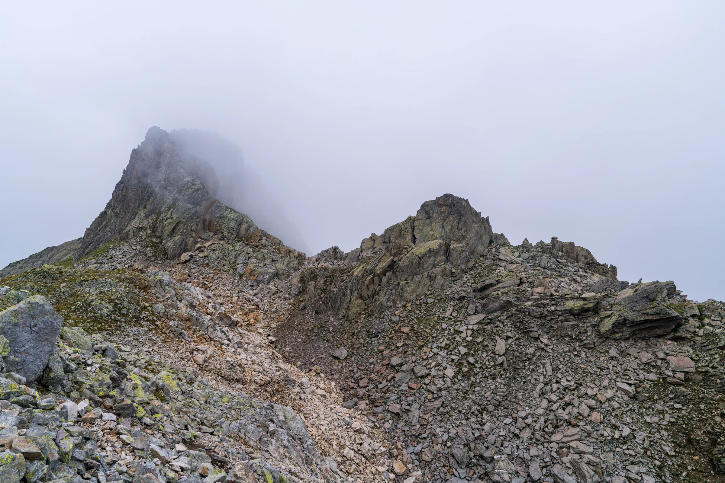 A rugged gray mountain ridge disappearing into low cloud above a rocky slope.