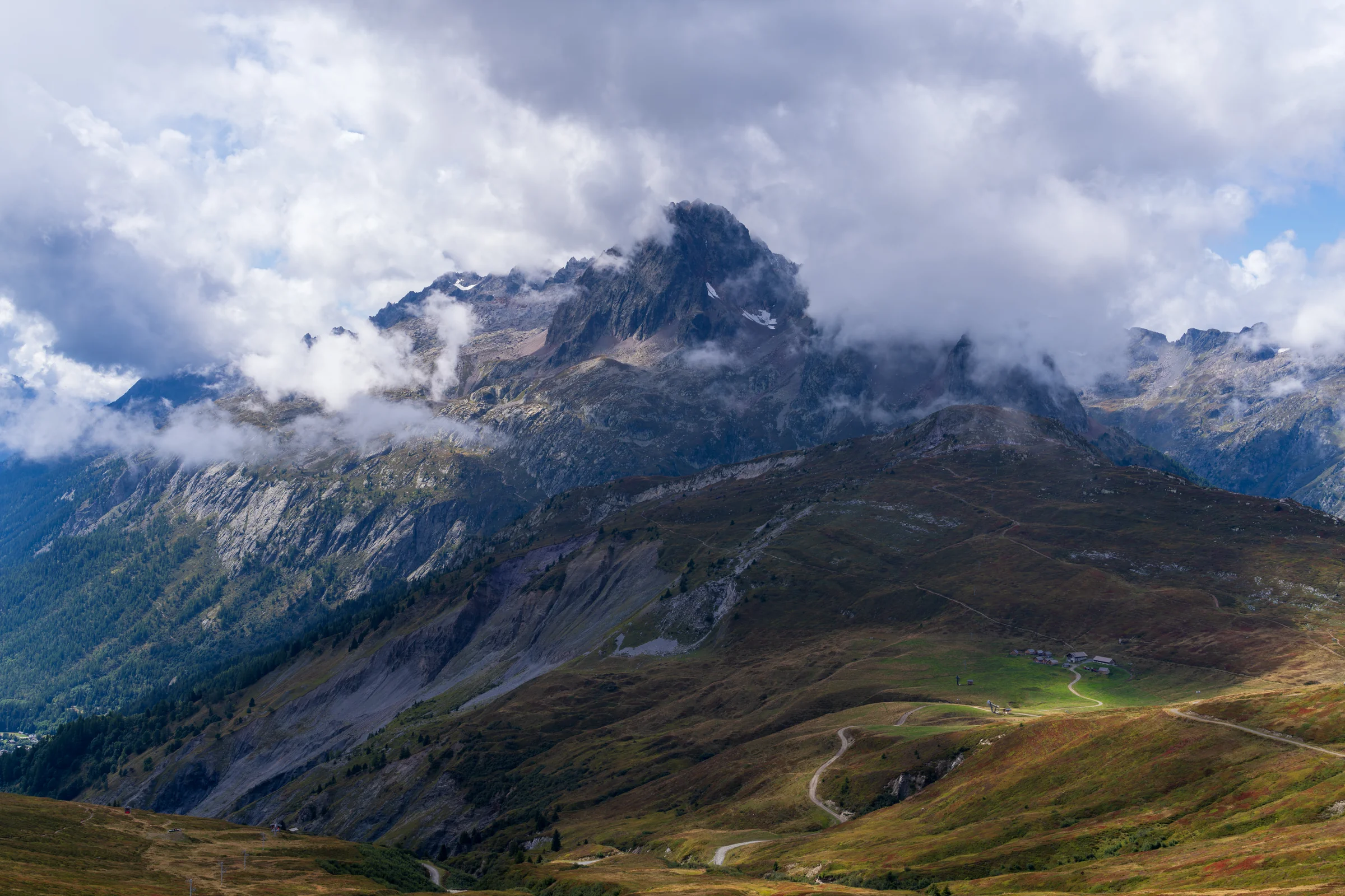 A dark jagged mountain peak surrounded by drifting clouds above green and gold valley slopes.
