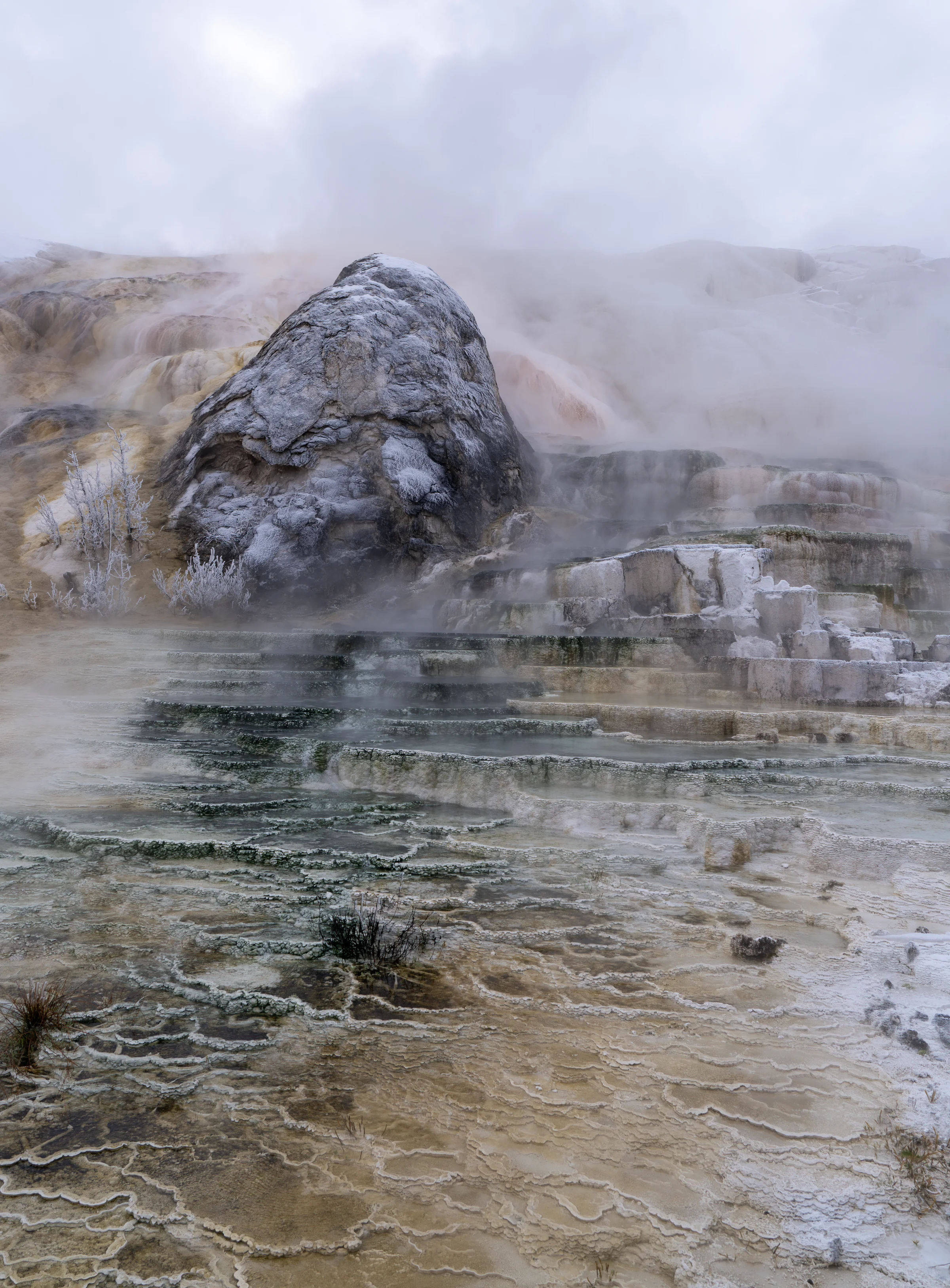 A rounded mineral-covered formation surrounded by steam and shallow water.