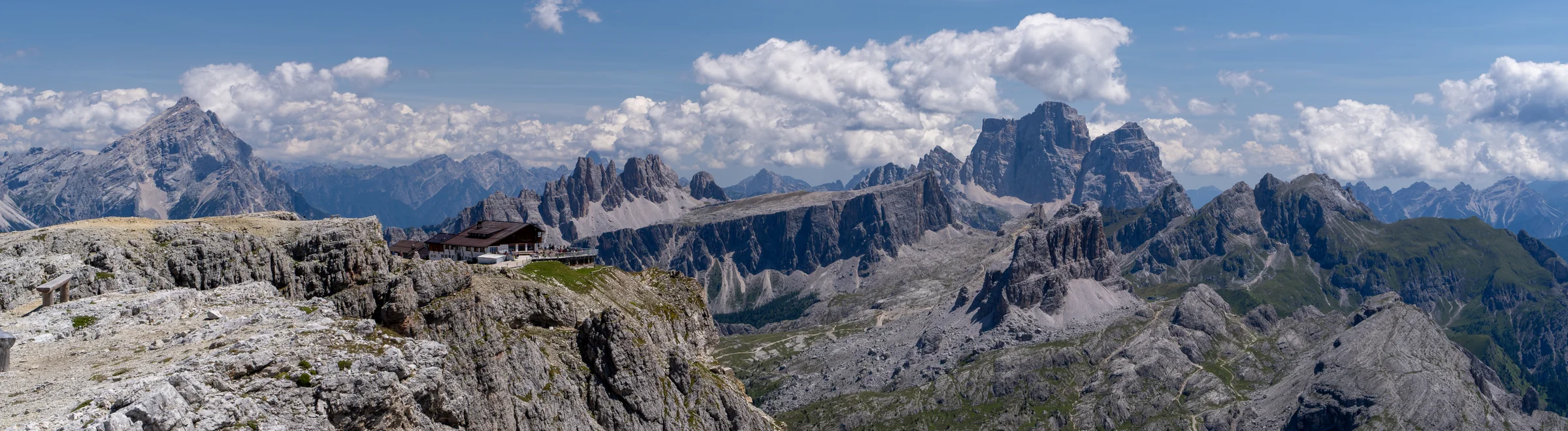 A wide panorama of jagged mountain summits and pale rocky ridges under a blue sky.