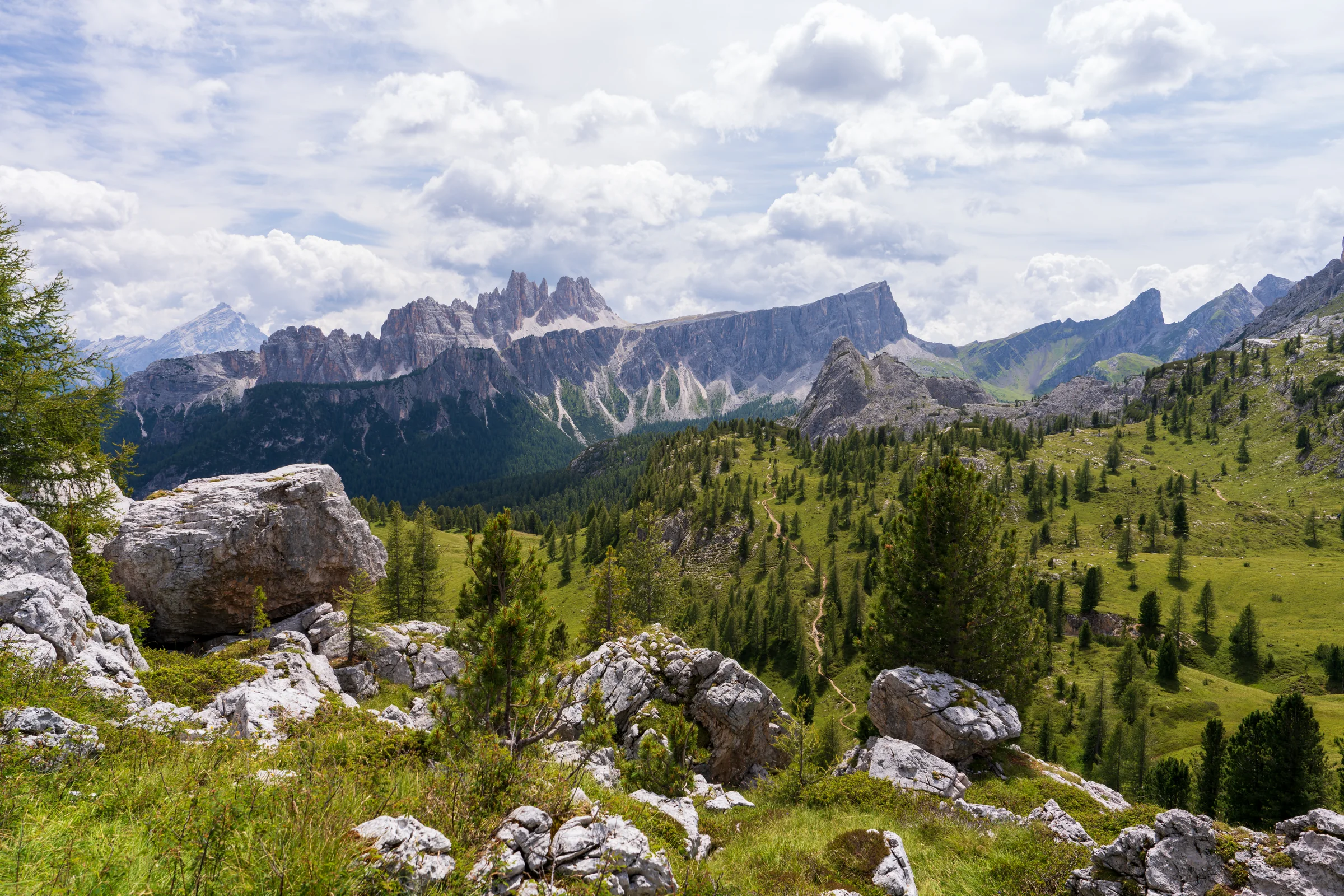 Pale boulders and green trees across a mountain slope with a rugged ridge beyond.