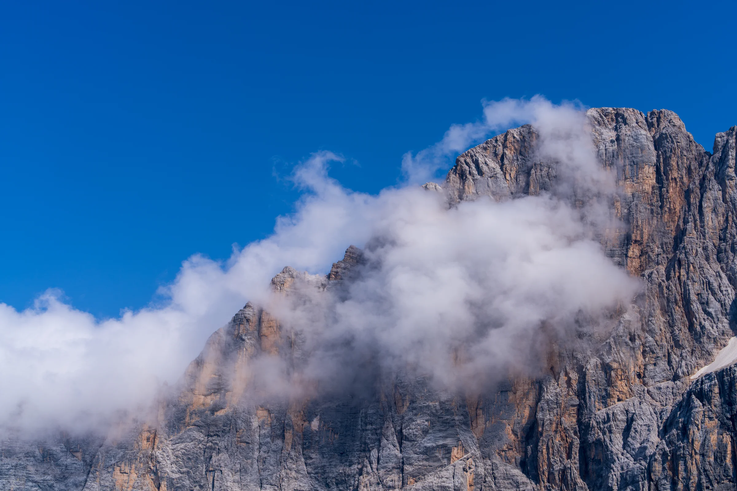 A steep gray rock face partly wrapped in white cloud beneath a deep blue sky.
